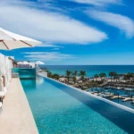 Piscina infinita de hotel boutique en Los Cabos con camastros, sombrillas y vista al mar y marina.